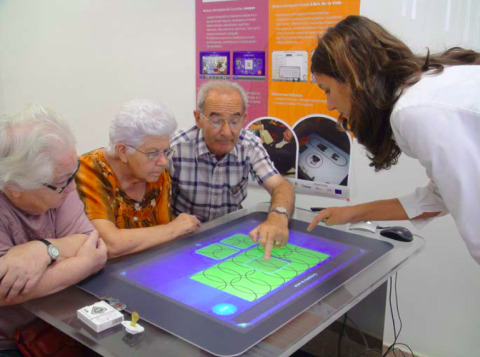 Sociable application being used by 3 elderly people and a carer giver, with everyone focusing on the board on the table.