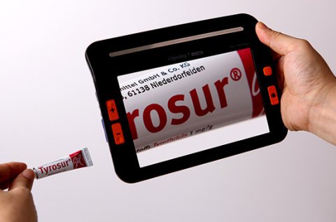 A black tablet-like device displaying magnified text from the small tube below it.