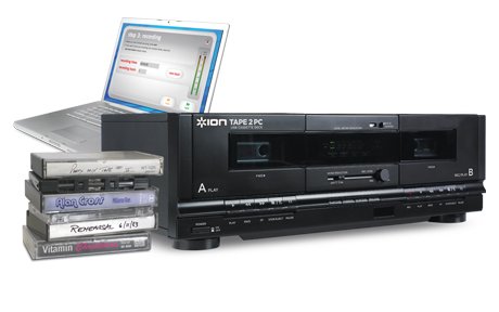 A large, black cassette player next to a stack of cassette tapes. Behind them is a silver laptop computer.